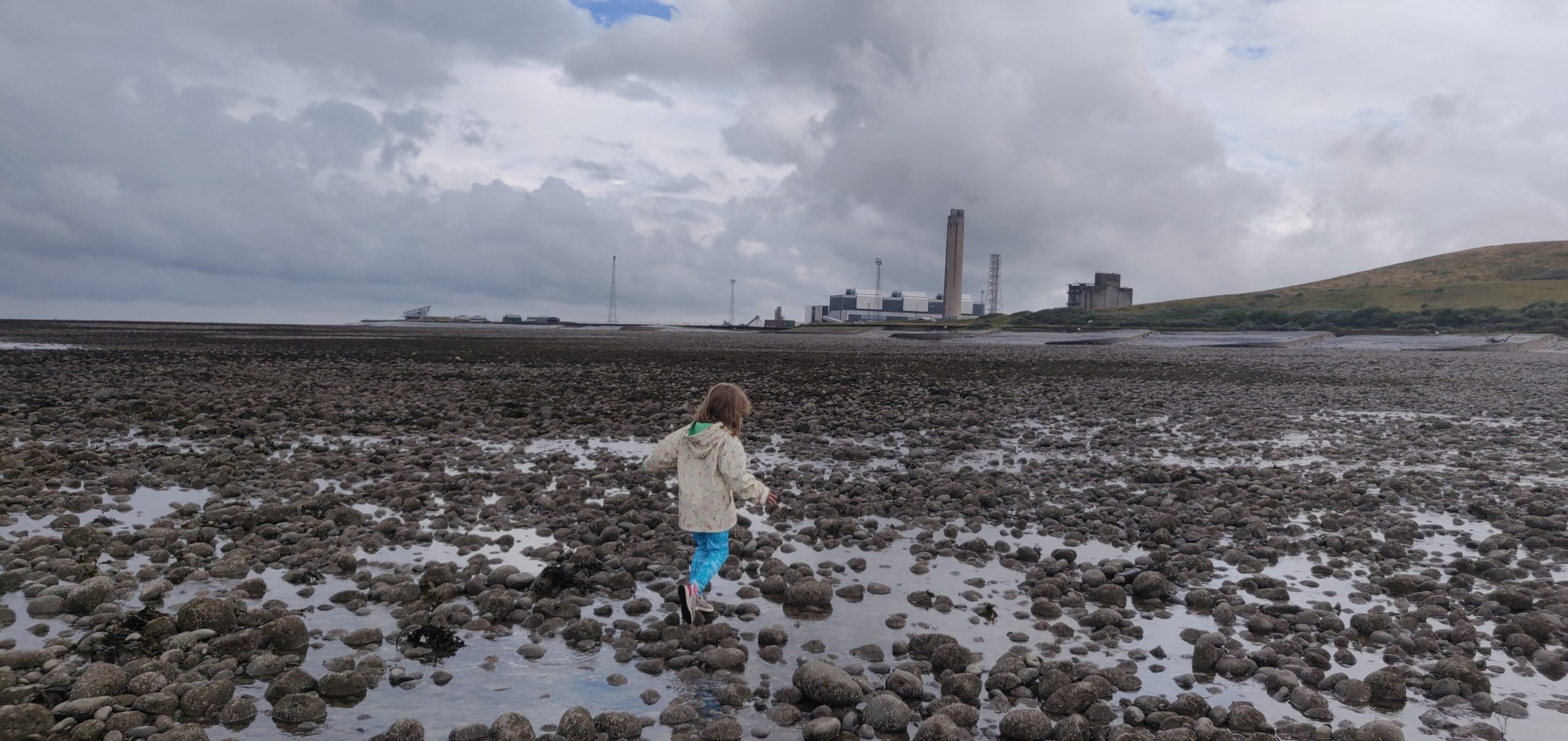 Girl walking on a stony beach with a power station behind